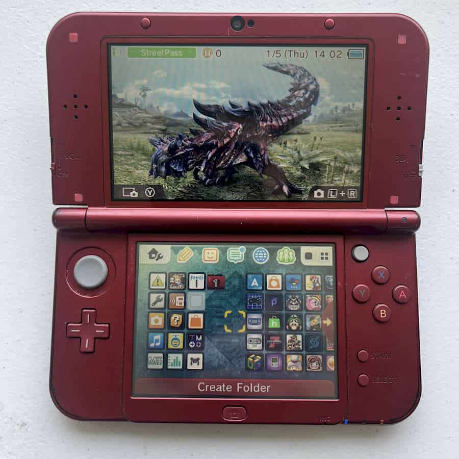 Red Nintendo 3DS XL with game screen and menu displayed.